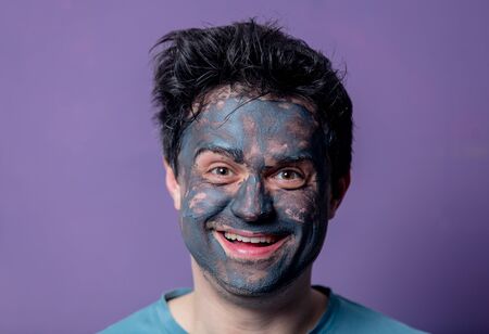 smiling guy in a face care mask on a purple background