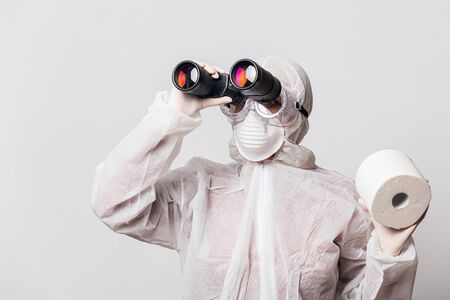 young doctor in protection suit and glasses with mask with toilet paper and binoculars on white backgroundの写真素材