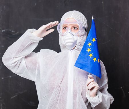 female doctor in protection suit and glasses with mask holds flag of EU