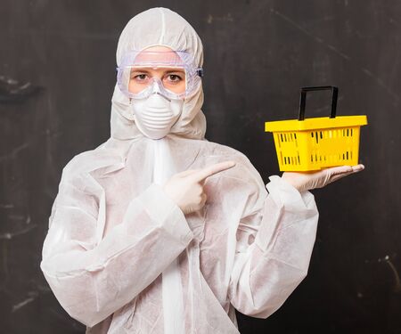 female in protection suit and glasses with mask holds shopping basketの写真素材