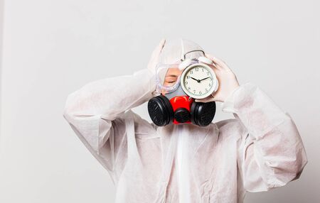 female doctor in protection suit and glasses with mask holds alarm clockの写真素材
