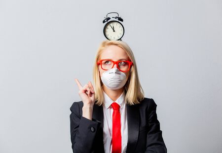 Businesswoman in face mask and red glasses with alarm clock on grey backgroundの写真素材