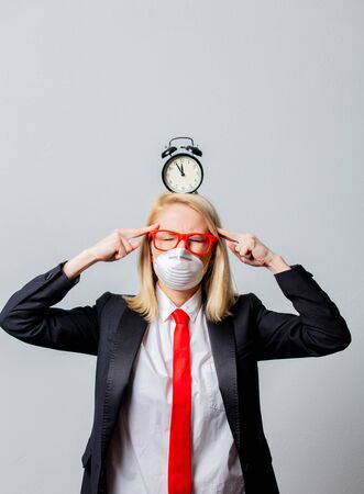 Businesswoman in face mask and red glasses with alarm clock on grey backgroundの写真素材