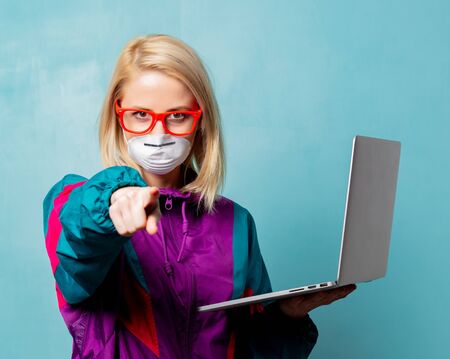 Style blonde woman in 90s clothes and face mask holds notebook on blue background