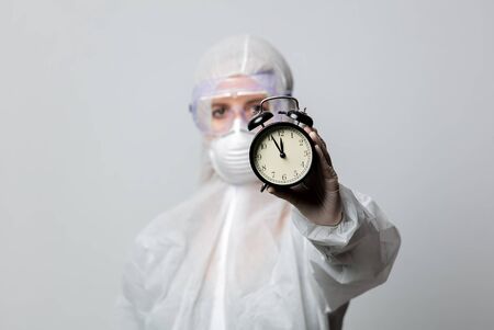 medic in protection clothes holds alarm clockの写真素材