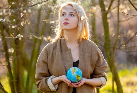 Blonde woman holds Earth globe in blooming cherry garden in sunset timeの写真素材