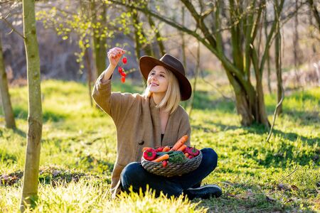 Blonde woman with vegetables in basket in blooming garden in spring timeの写真素材
