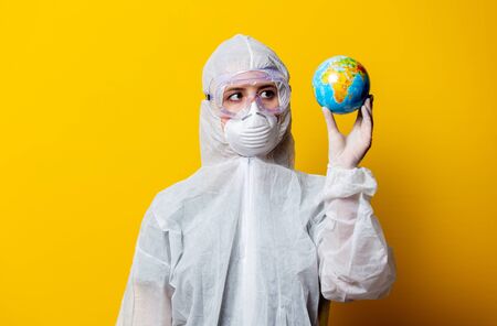 Medic in protection suit and mask hold Earth globe on yellow background