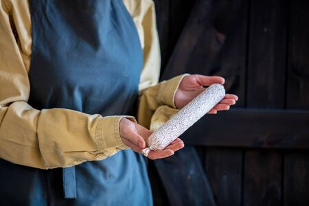 Woman in apron holds salami in handsの写真素材