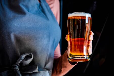 brewer in apron holds glass of beerの写真素材
