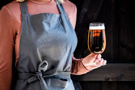 brewer in apron holds glass of beerの写真素材