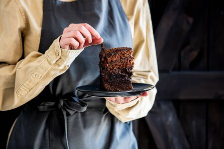 Pastry chef in apron holds chocolate cake