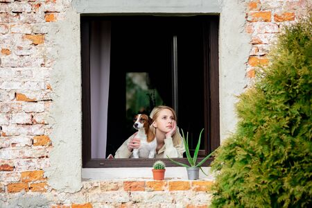 woman with a dog sits at the window during quarantine