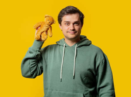Guy in green hoodie with teddy bear on yellow backgroundの写真素材