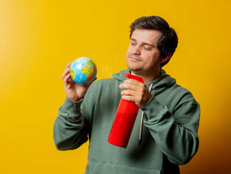 Man with Earth globe and disinfection spray on yellow backgroundの写真素材