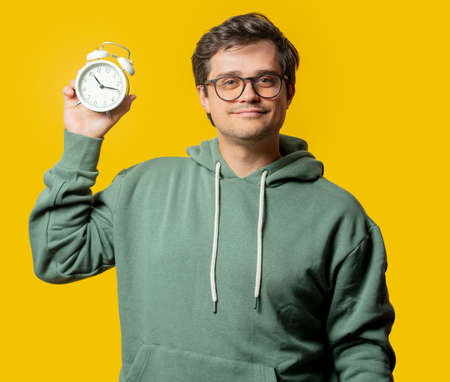 man in green hoodie hold alarm clock on yellow backgroundの写真素材