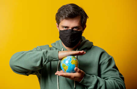 guy in facemask hold Earth globe on yellow background