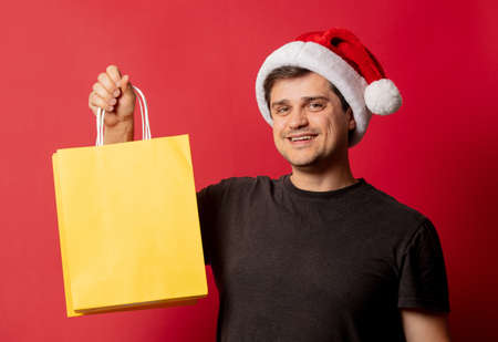 Man in Christmas hat and black t-shirt with shopping bags on red backgroundの写真素材