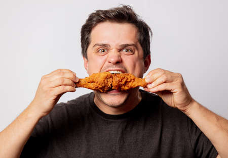 White man in black shirt with chicken drumsticks on white backgroundの写真素材