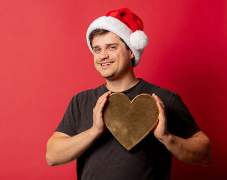 Brunette guy in Christmas hat with heart shape on red backgroundの写真素材