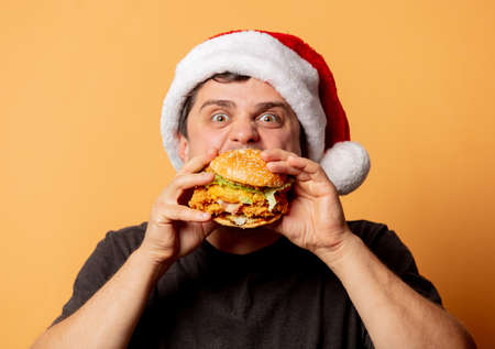 White man in black shirt and Santa Claus hat with burger on yellow backgroundの写真素材