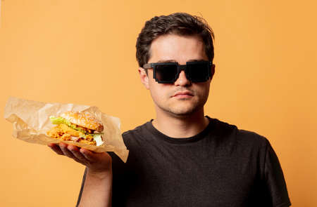 White man in black shirt with burger on yellow background