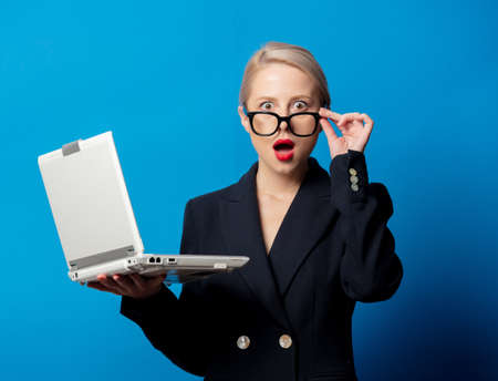 Style blonde in black jacket with notebook computer on blue backgroundの写真素材