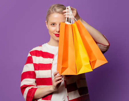 Beautiful blonde in red jacket with shopping bags on puprle background