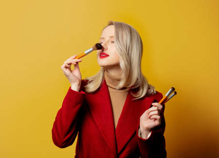 Beautiful woman in red coat with brushes on yellow backgroundの写真素材