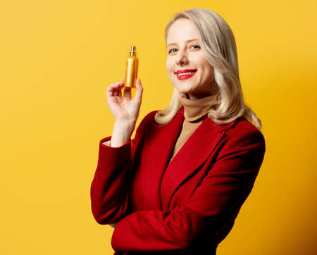 woman in red coat with perfume on yellow backgroundの写真素材