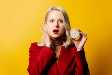 woman in red coat with cream jar on yellow background