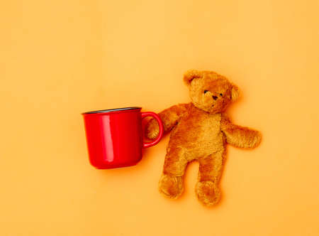 Red cup of coffee and tedd bear on yellow backgroundの写真素材