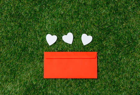 Three heart shapes and red envelope on green grass.