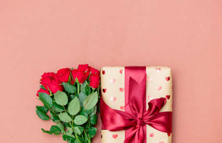 Bouquet of red roses and gift box on pink background. Above view