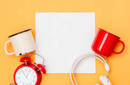 White mockup board and cup of coffee with alarm clock and headphones on yellow background