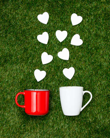 Two cups of coffee and heart shapes on green grass. Above view