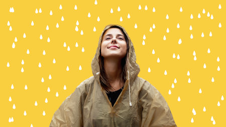 Young woman in raincoat with painted drops on yellow backgroundの写真素材