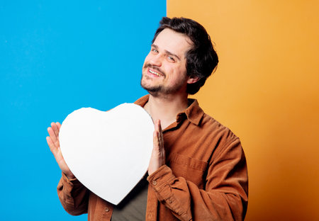 Guy in shirt hold heart shape banner on yellow and blue backgroundの写真素材