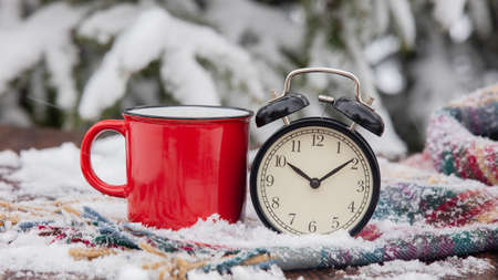 Red cup of coffee and vintage alarm clock with scarf on wooden table in blizzardの写真素材