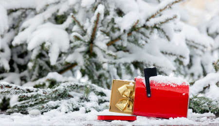 Red mailbox with gift box inside on wooden table in snowの写真素材