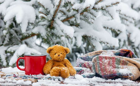 Red cup of coffee and scarf with teddy bear on wooden table in blizzardの写真素材