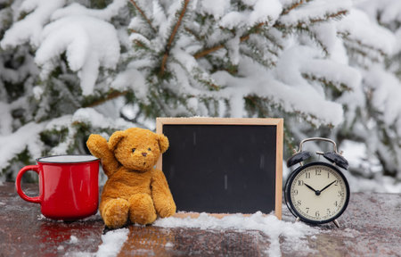 Teddy bear and blackboard with alarm clock on wooden table in blizzard