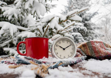 Red cup of coffee and vintage alarm clock with scarf on wooden table in blizzard