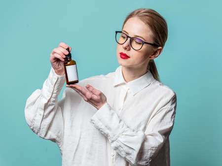 Portrait of beautiful blonde in white shirt with cosmetic bottle on blue backgroundの写真素材