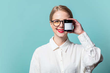 Portrait of beautiful blonde in white shirt with cream jat on blue background