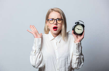 Portrait of beautiful blonde in white shirt with alarm clock on white background