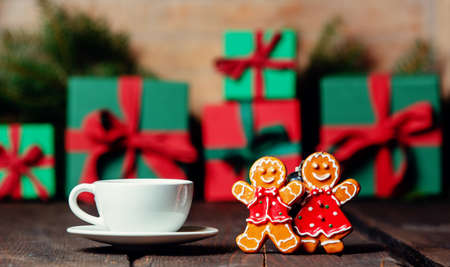 Cup of coffee and gingerbread man and woman next to Christmas gifts on wooden tableの写真素材