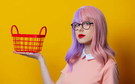 Girl with purple hair and pink dress with red shopping basket on yellow backgroundの写真素材
