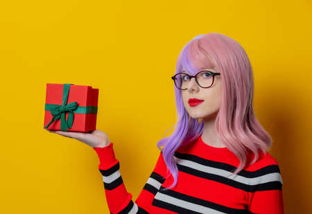 girl with purple hair in red striped sweater with gift box on yellow backgroundの写真素材