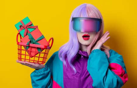 Style woman in VR glasses and 90s sport suit hold basket with gift boxes on yellow backgroundの写真素材